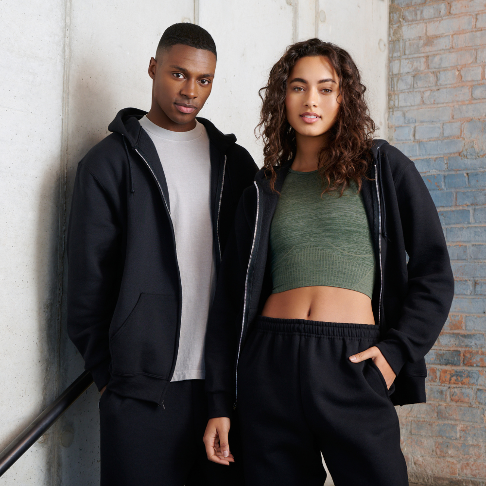 male model wearing white t-shirt, black zip hoodie sweatshirt and black sweatpants, female model wearing green top, black zip hoodie sweatshirt and black sweatpants